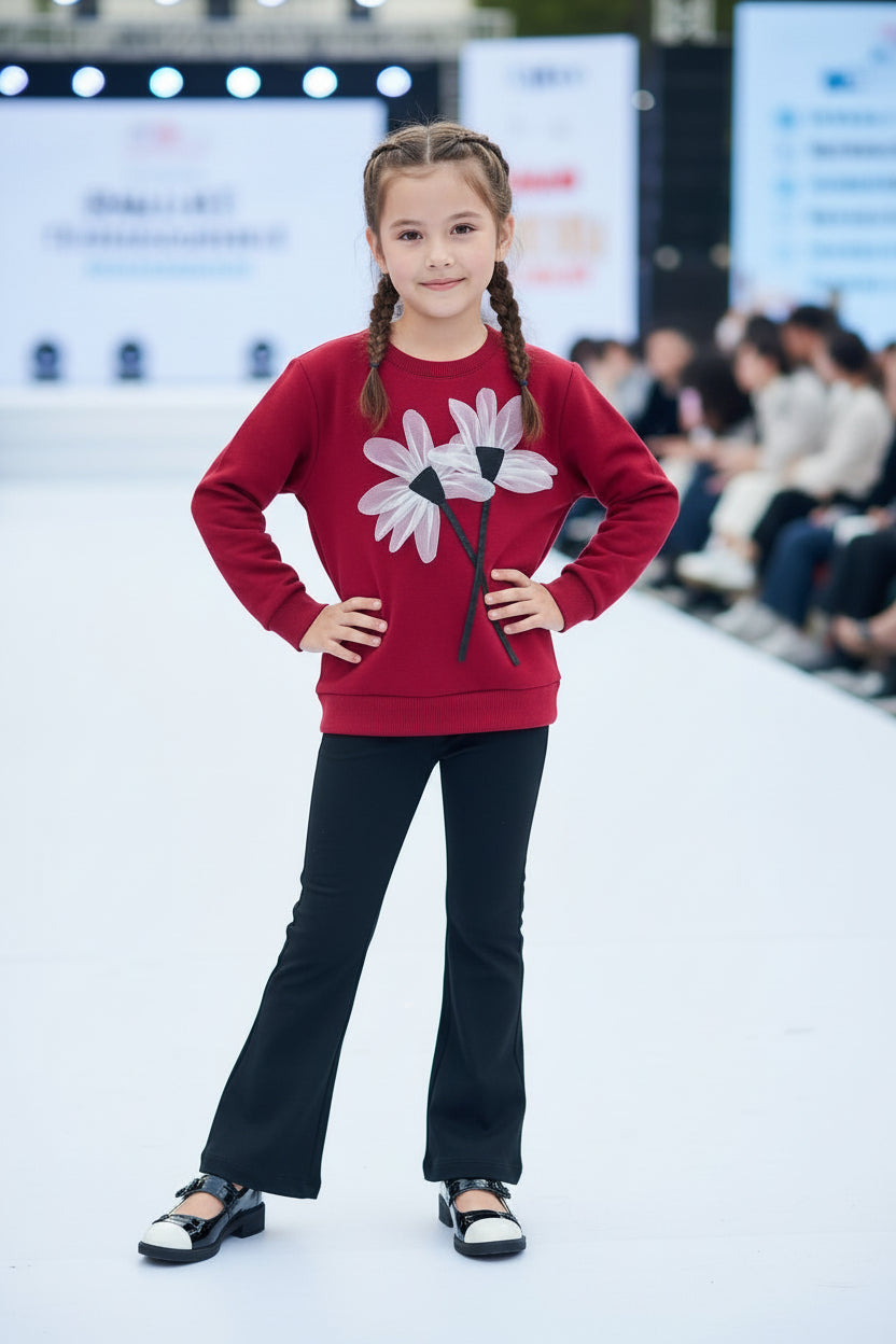 Child model wearing a red sweater with a floral design on a fashion show runway.
